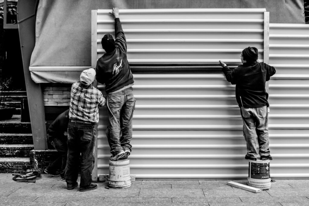 grayscale photo of three men arranging metal wall